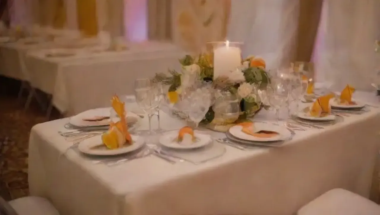 Mesa elegantemente decorada con manteles blancos, cubiertos de plata, copas de cristal, flores suaves y velas