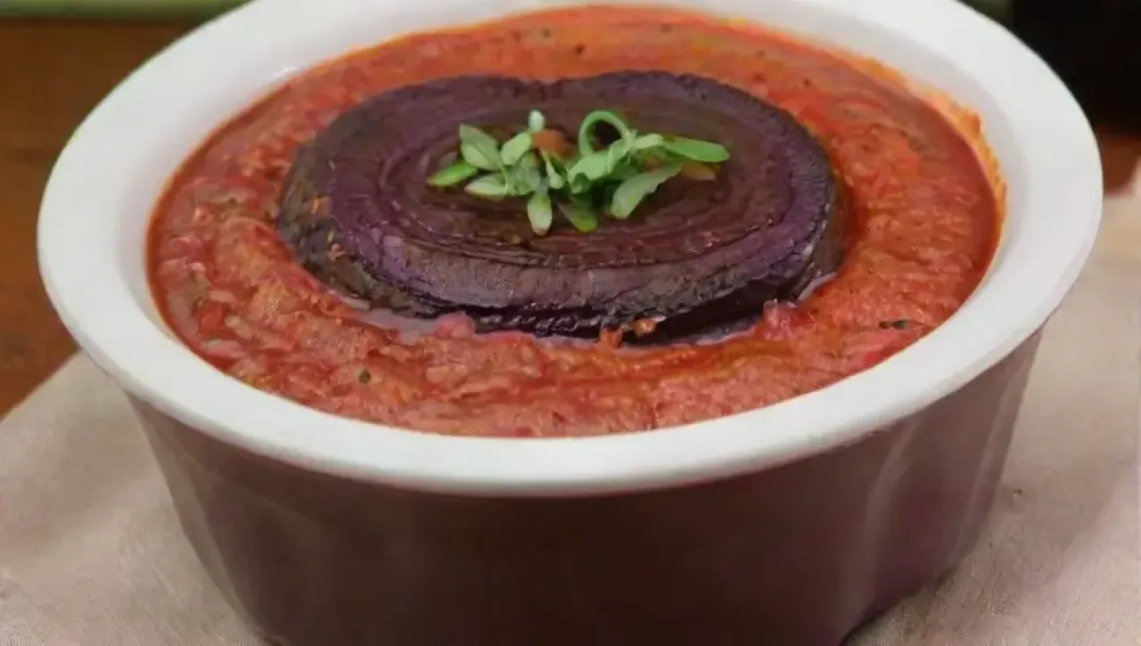 Un festín visual de berenjenas moradas, calabacines dorados, salsa de tomate, bechamel, queso feta y aceitunas, servido en un ambiente acogedor