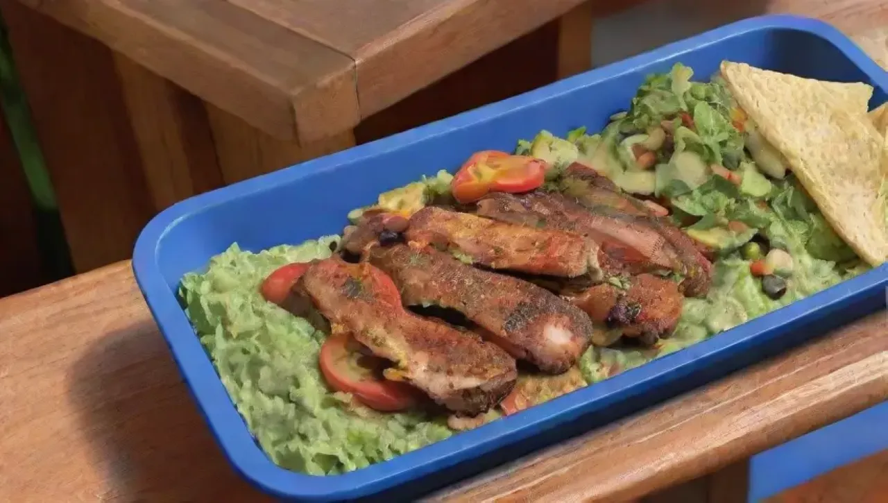 Una colorida escena culinaria con ensalada, pollo, guacamole y salsa en un ambiente acogedor
