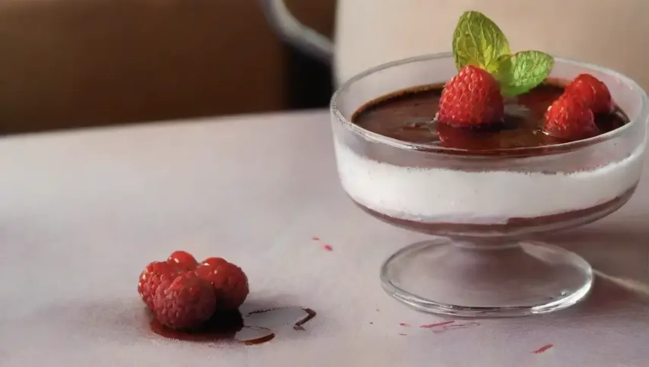 Un elegante postre de gelatina de chocolate con frutas y crema, rodeado de un ambiente acogedor