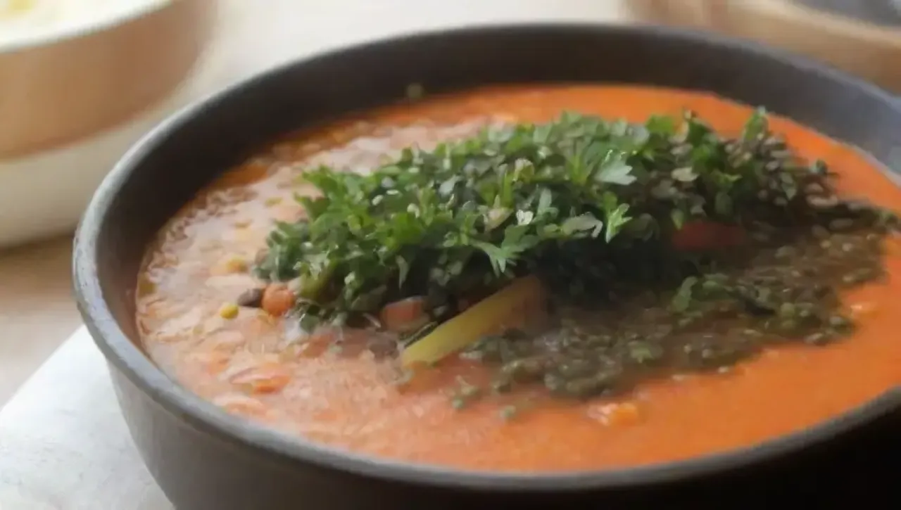 Un tazón de sopa de lentejas con zanahorias y hierbas frescas en una mesa rústica