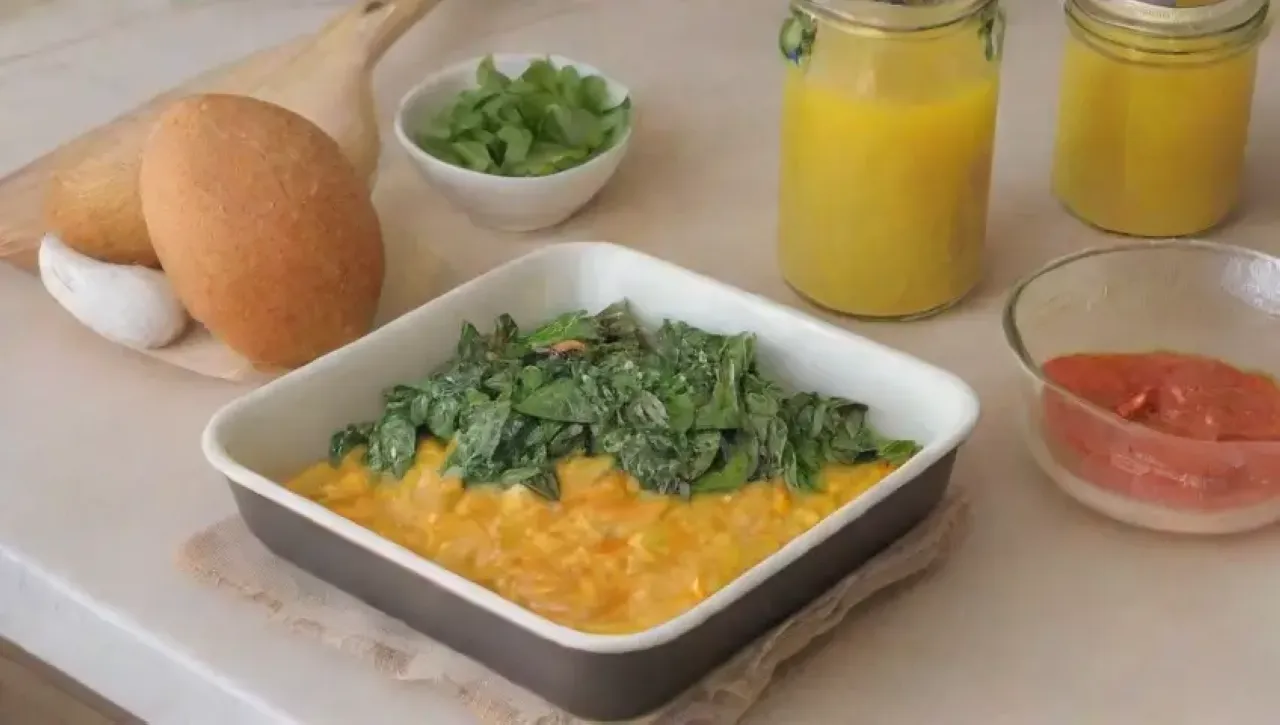 Cocina luminosa con espinacas frescas, huevos, especias y un plato colorido en un ambiente acogedor