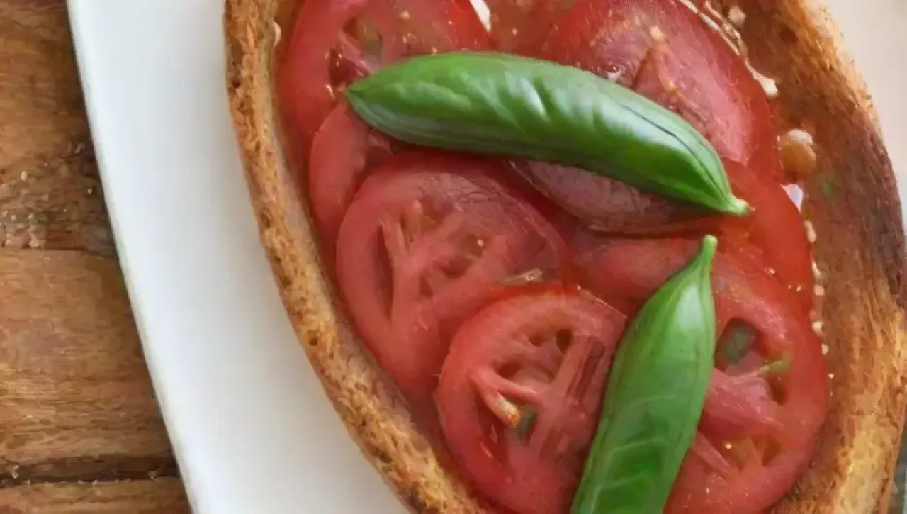 Un festín visual de tomates rojos, albahaca fresca, pan dorado, aceite de oliva, sal marina y otros ingredientes dispuestos artísticamente
