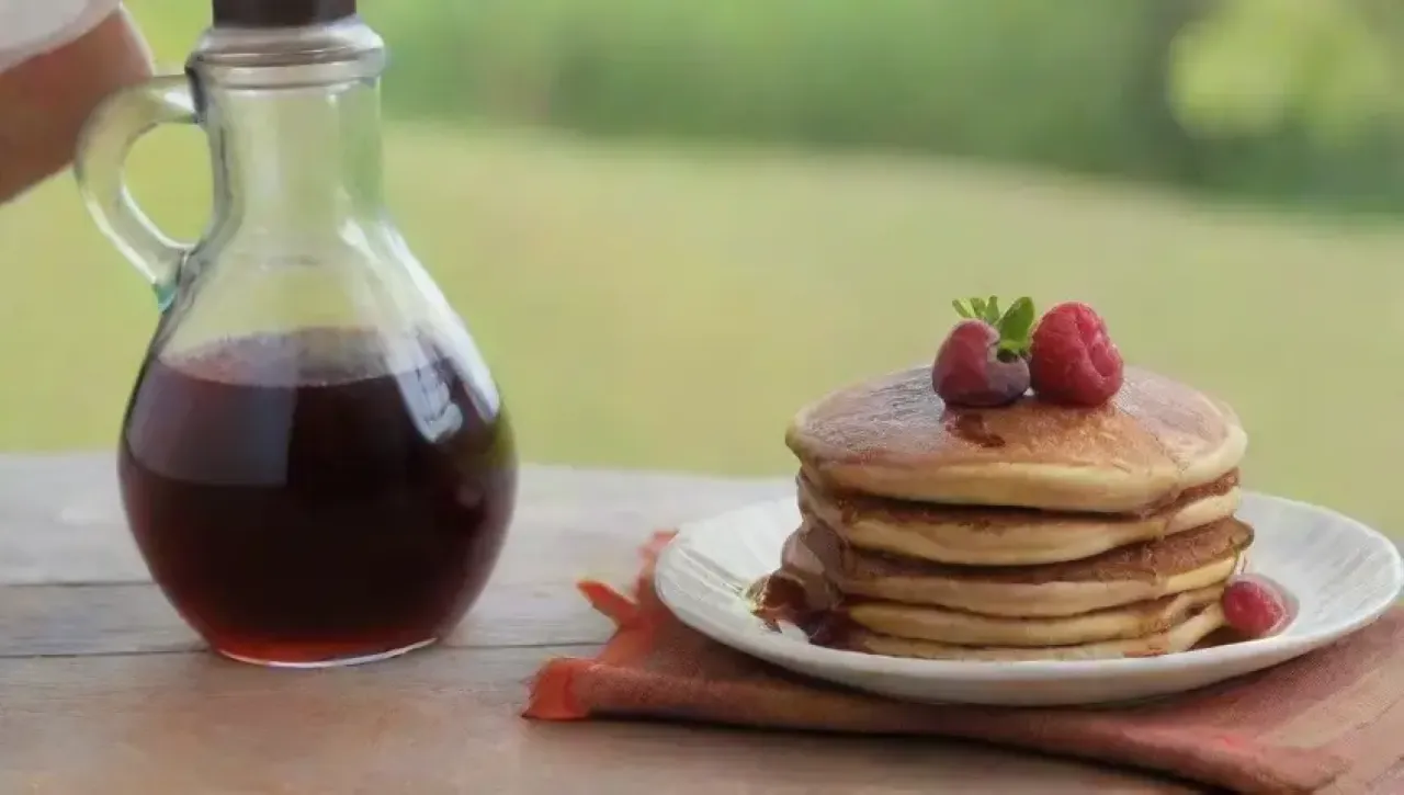 Botella de jarabe de arce junto a pancakes dorados, frutas frescas y un ambiente acogedor