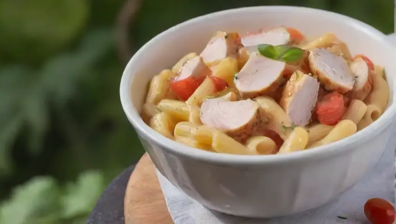 Un delicioso plato de pasta con salsa cremosa, pollo tierno, albahaca fresca y queso parmesano
