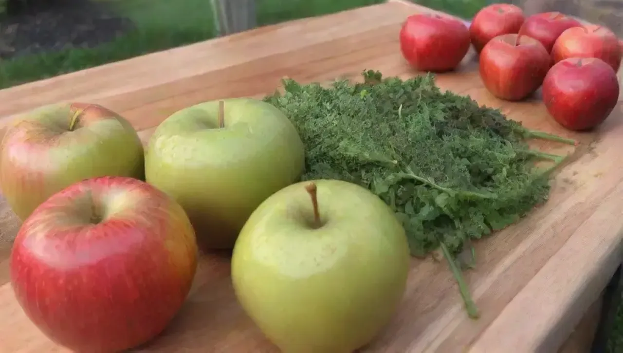 Raíces de jengibre verdes y frescas, manzanas rojas brillantes y un jugo dorado en una cocina rústica iluminada por el sol