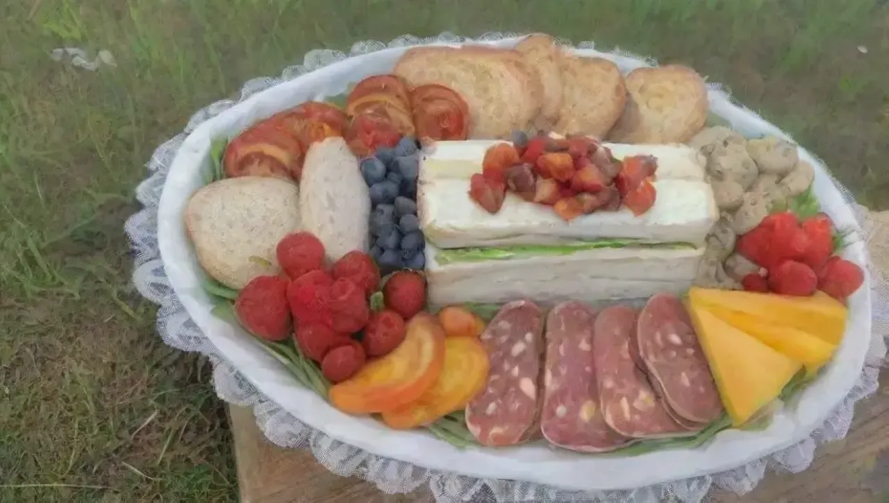 Un picnic gourmet vibrante en un césped verde, con quesos, vino, frutas y risas
