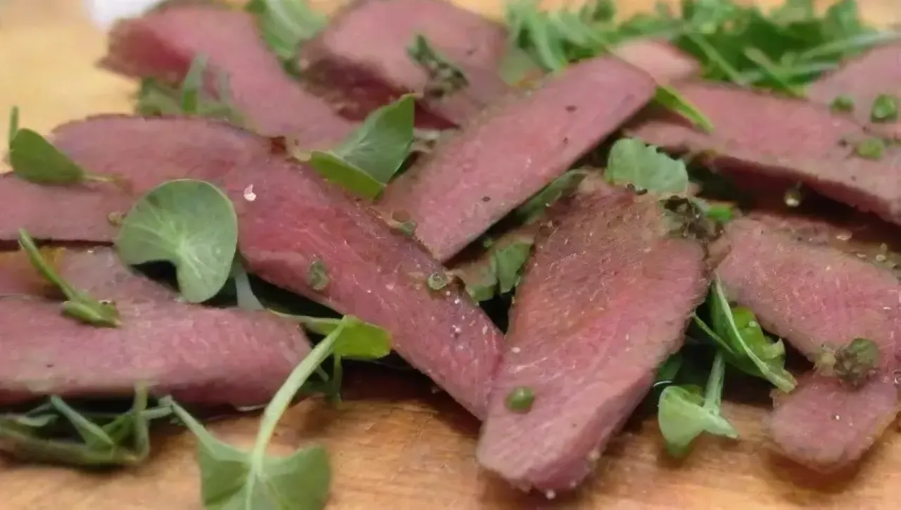 Finas lonchas de carne roja con sal, pimienta, rúcula, parmesano, reducción de balsámico y aceite de oliva, listas para disfrutar