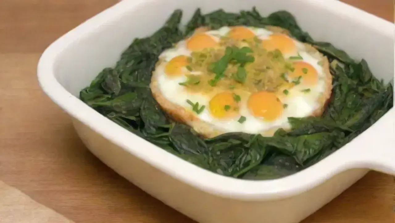 Un plato de espinacas y huevos dorados, listo para servir, con hierbas frescas y un tenedor al lado