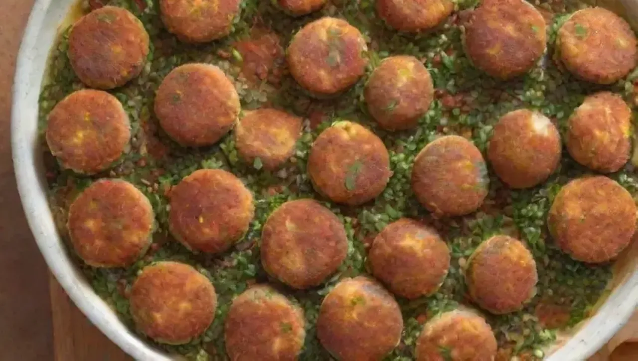 Un plato de croquetas doradas y crujientes, acompañadas de hierbas frescas, mayonesa vegana y especias coloridas, evoca calidez y sabor