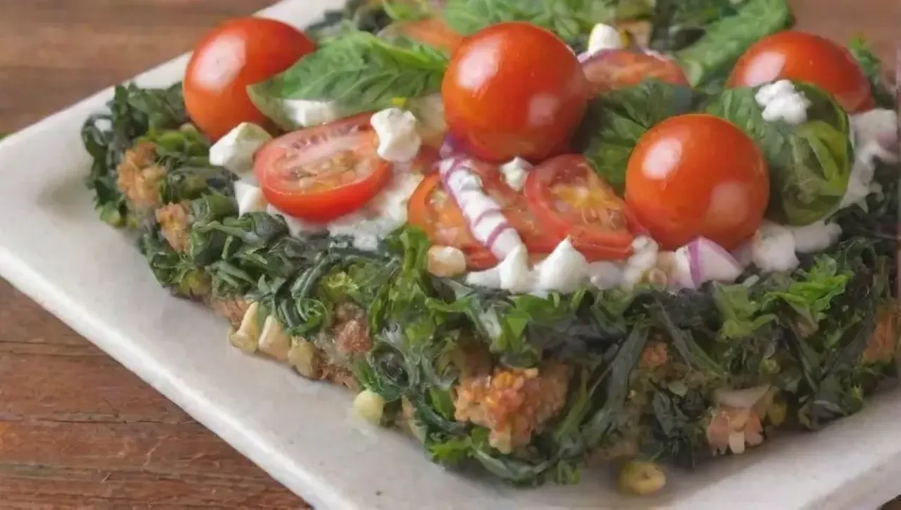 En un tazón rústico, kale verde, tomates cherry, cebolla roja, queso feta, piñones, aceite de oliva, limón, sal, albahaca, y flores crean un ambiente alegre y vibrante