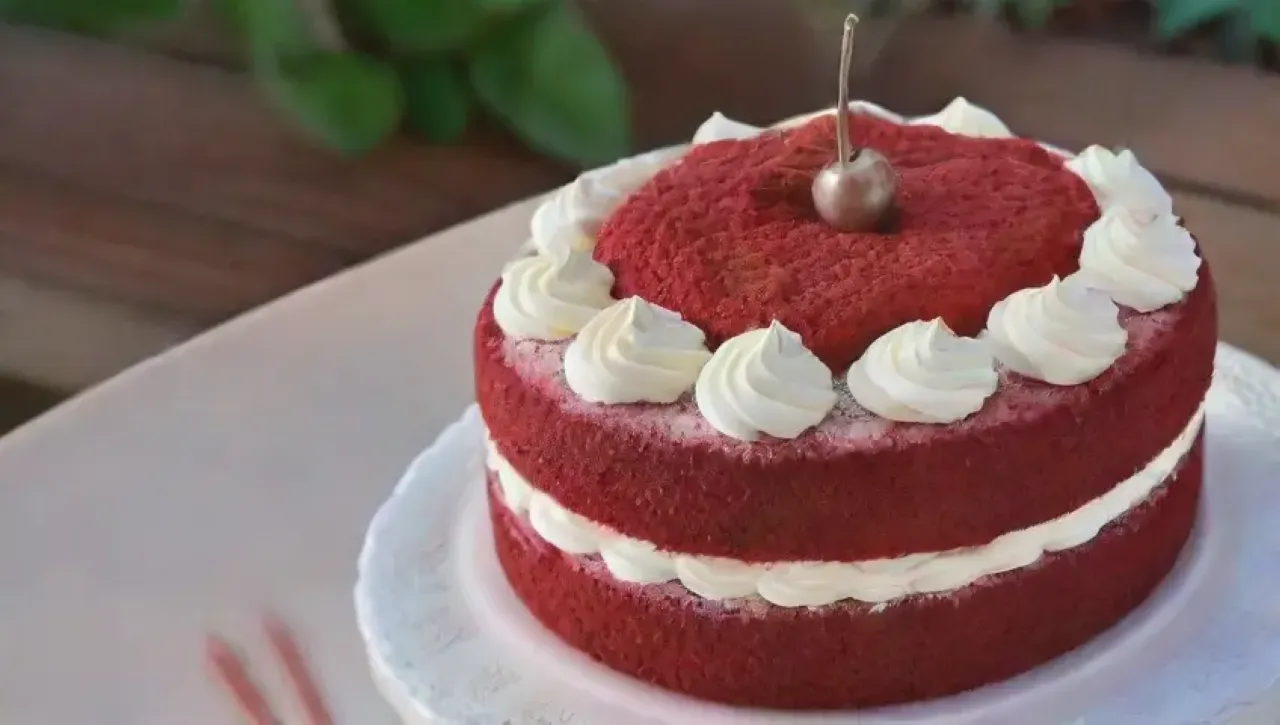 Un festín visual de un vibrante pastel de terciopelo rojo con crema de queso y decoraciones coloridas en un ambiente acogedor