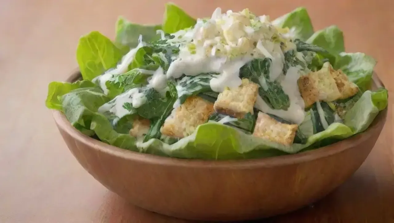 Ensalada César vibrante y fresca, con lechuga romana, aderezo cremoso, crutones dorados, queso parmesano, limón y hierbas, presentada elegantemente