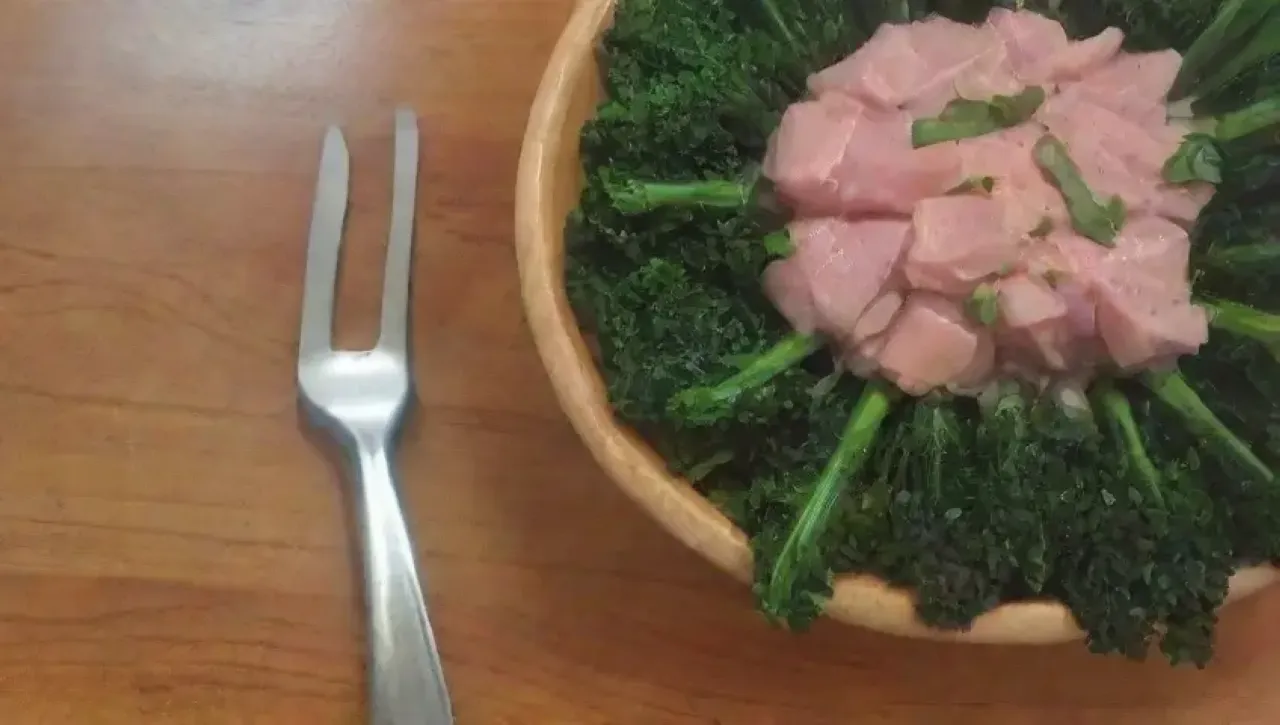 Un tazón de col rizada fresca y crujiente con trozos de jamón ahumado, sopa humeante y pan crujiente en una cocina acogedora