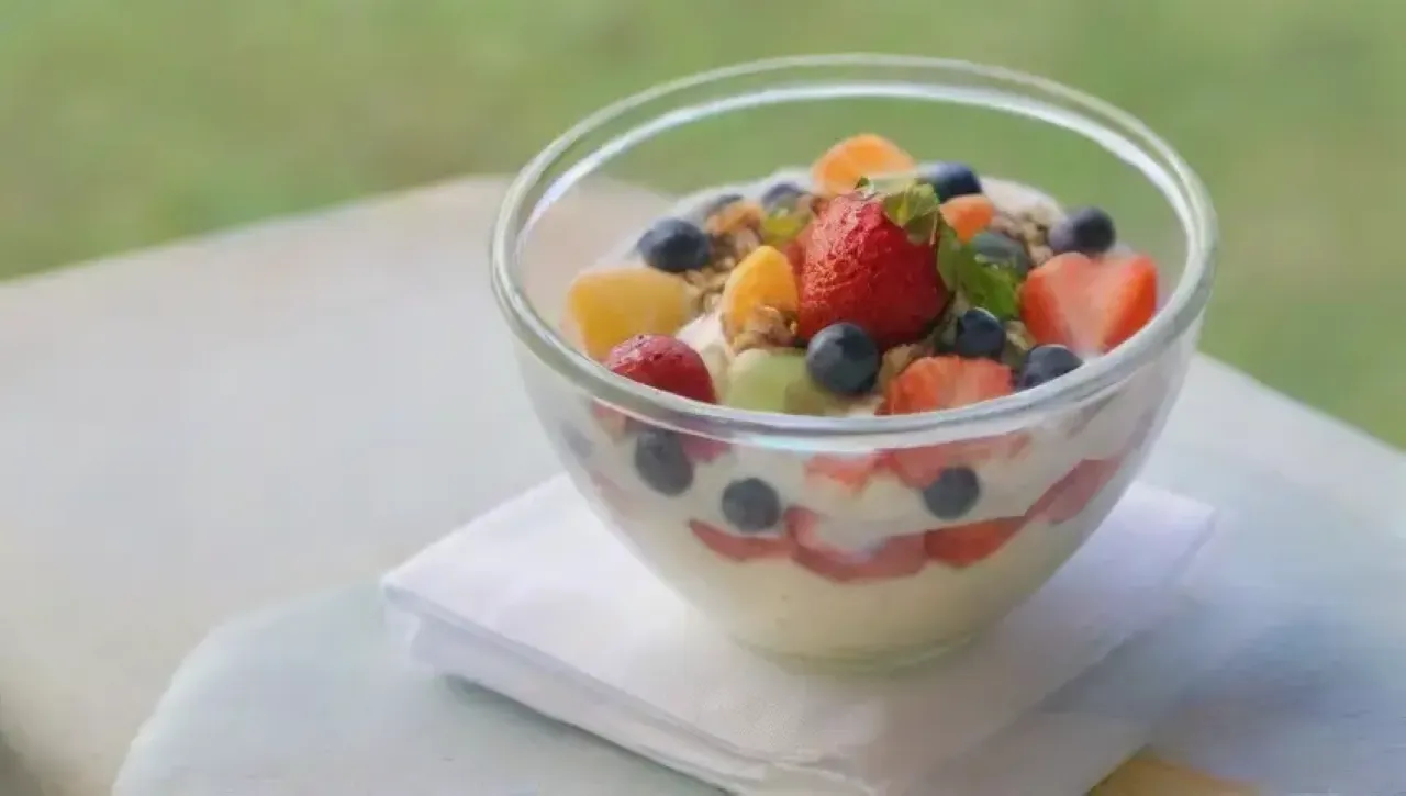 Frutas coloridas con yogur y granola en un vaso, iluminadas por la luz suave de verano