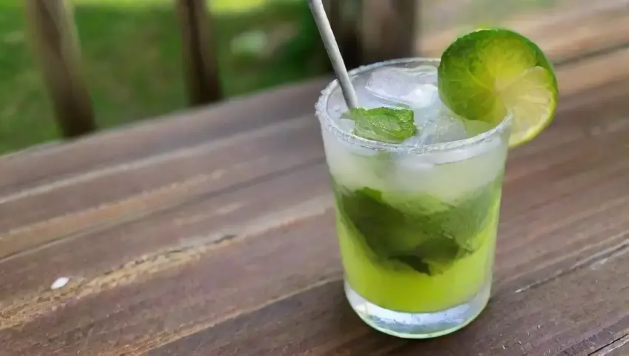Un refrescante mojito sorbete en un vaso, adornado con hojas de menta y rodajas de lima, evoca la esencia del verano