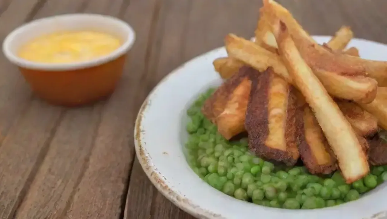 Papas fritas crujientes y pescado dorado, acompañados de guisantes y salsa tártara, en un ambiente costero acogedor