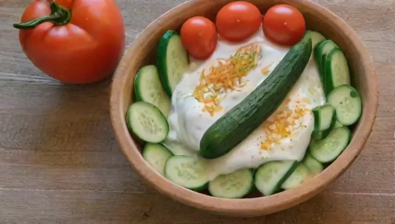 En un ambiente soleado de cocina, se presenta una fresca y colorida ensalada de pepinos con yogur, menta y tomates