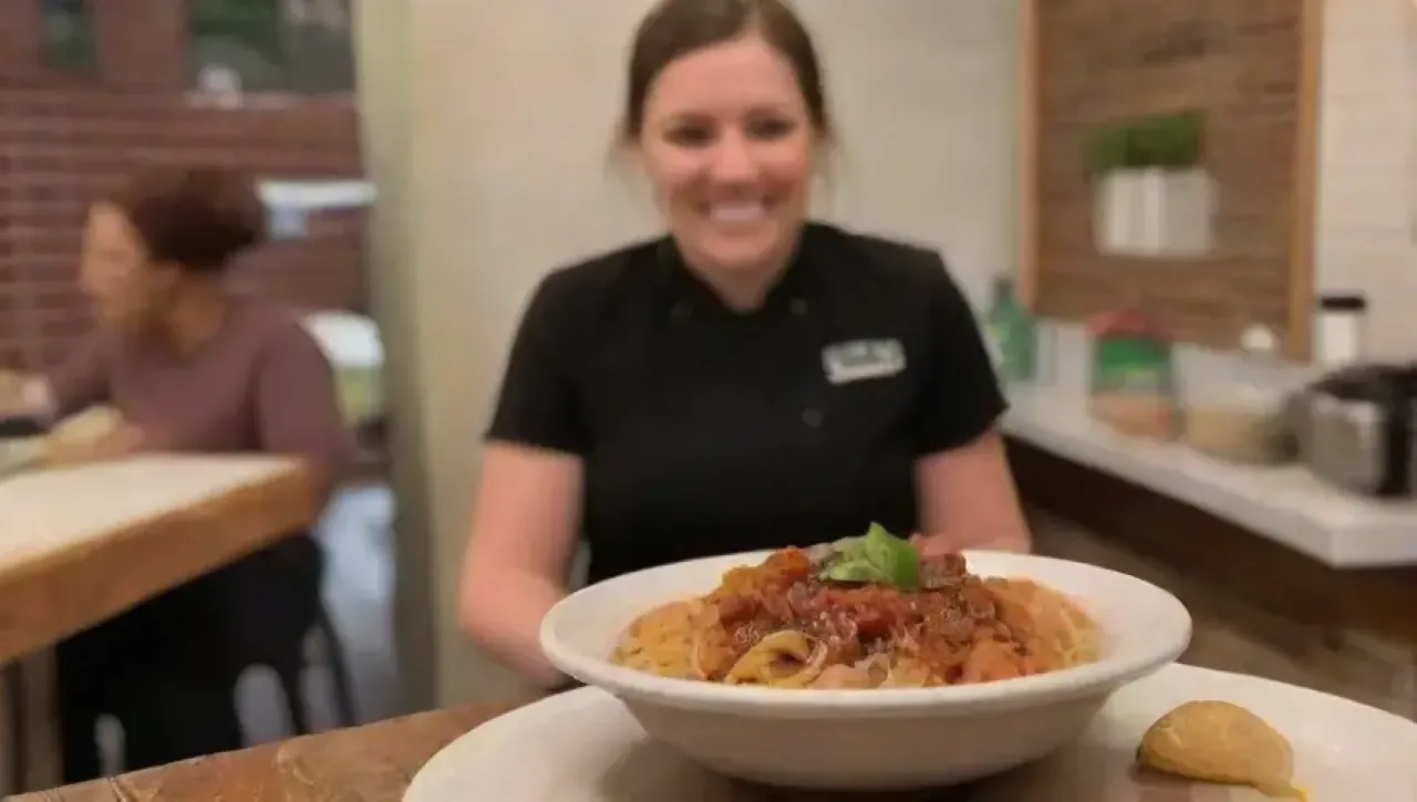 Un acogedor bistró con mesas de madera, luz suave, plantas verdes, cocina bulliciosa y deliciosos platos de pasta