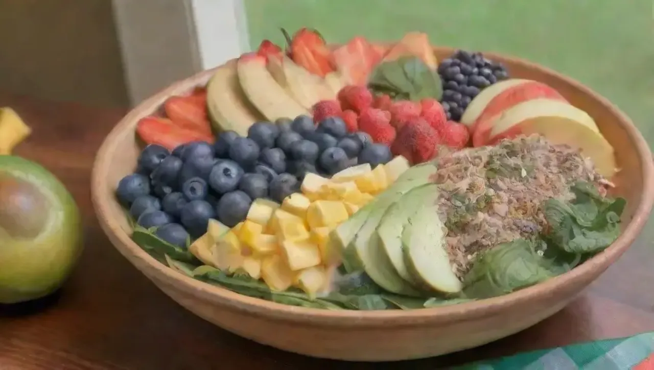 Una mesa de madera llena de frutas vibrantes y coloridas, smoothies y un ambiente tropical