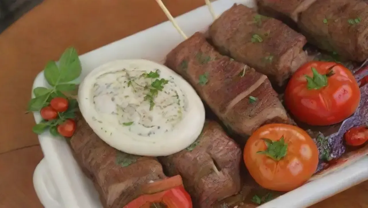 Brochetas de cordero especiadas con hierbas frescas y salsa de yogur, en un ambiente festivo