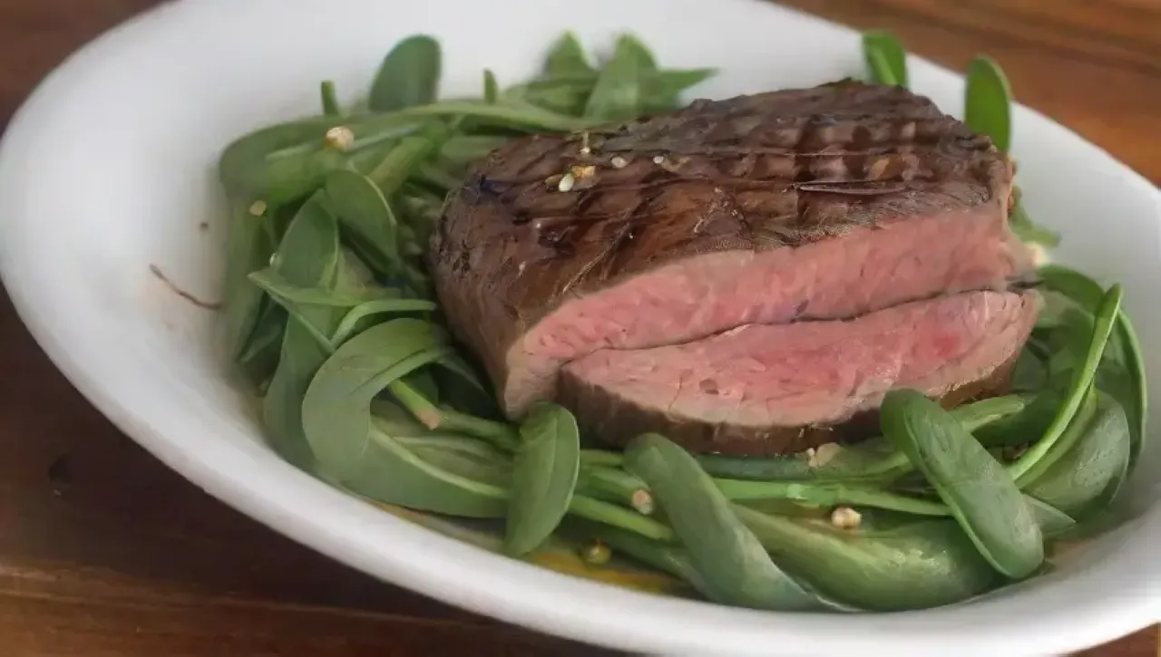 Una mesa rústica presenta un plato elegante de solomillo con arúgula, parmesano, aceite de oliva, limón y vino en un ambiente acogedor