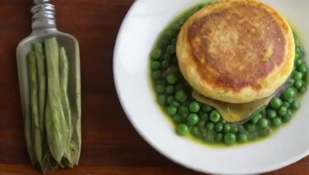 Un plato colorido y aromático de omelet con guisantes, cebolla caramelizada y hierbas frescas, servido en un ambiente acogedor