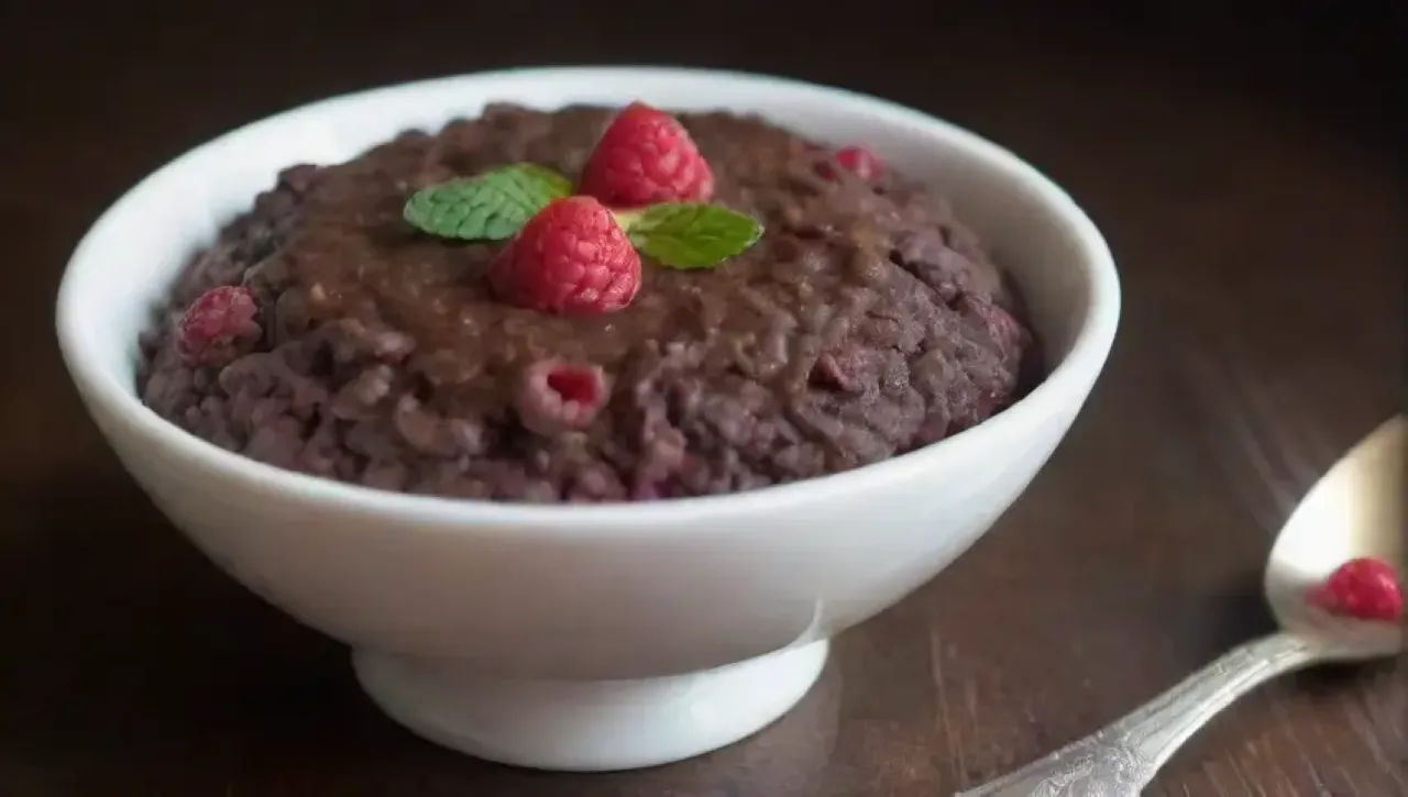 Un risotto de chocolate oscuro y cremoso, decorado con frambuesas, menta y un toque de oro comestible, en un ambiente acogedor