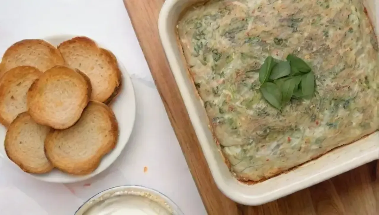 Dip de alcachofa cremoso con pan tostado y verduras, ideal para una reunión entre amigos