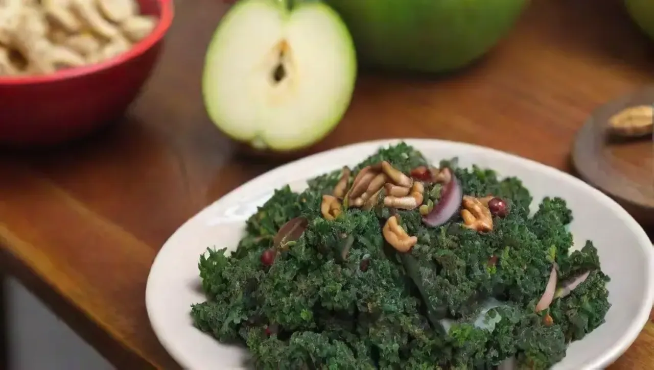 En un acogedor tazón de madera, se presenta una colorida ensalada de kale, manzana, nueces y granada, aderezada con aceite de oliva y limón