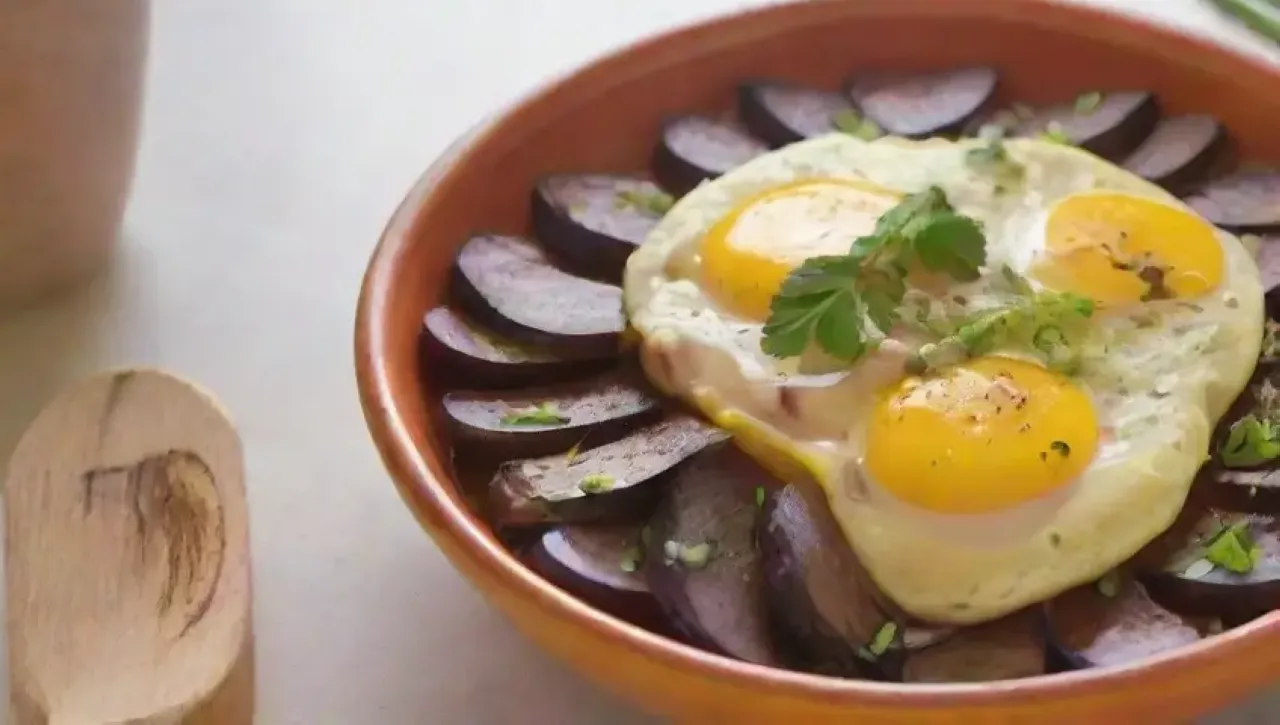 Una escena de desayuno perfecta con berenjenas moradas, huevos batidos, hierbas frescas y una omelet dorada en un plato